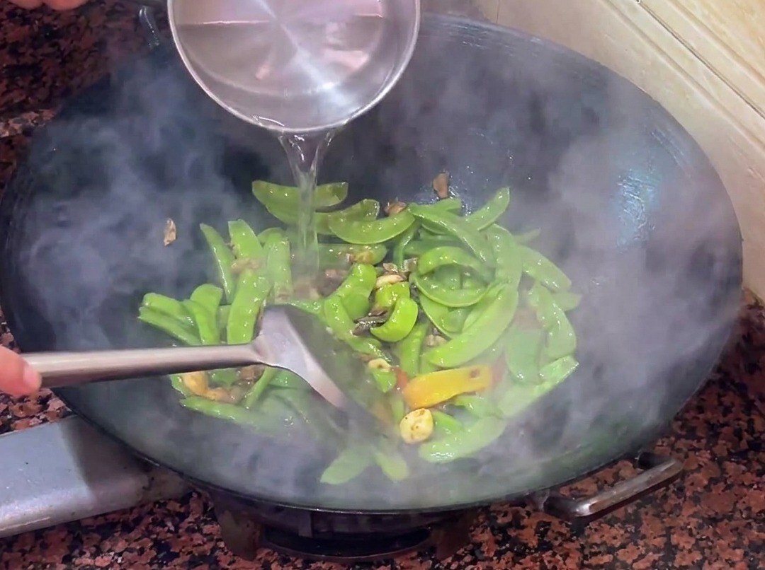 Acqua calda versata nel wok con le taccole e la salsiccia.