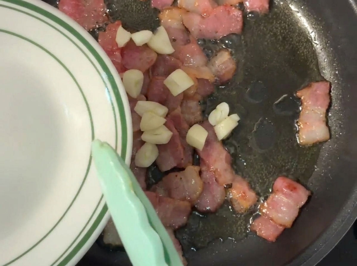 Aglio tritato appena aggiunto in padella accanto alla pancetta sfrigolante.