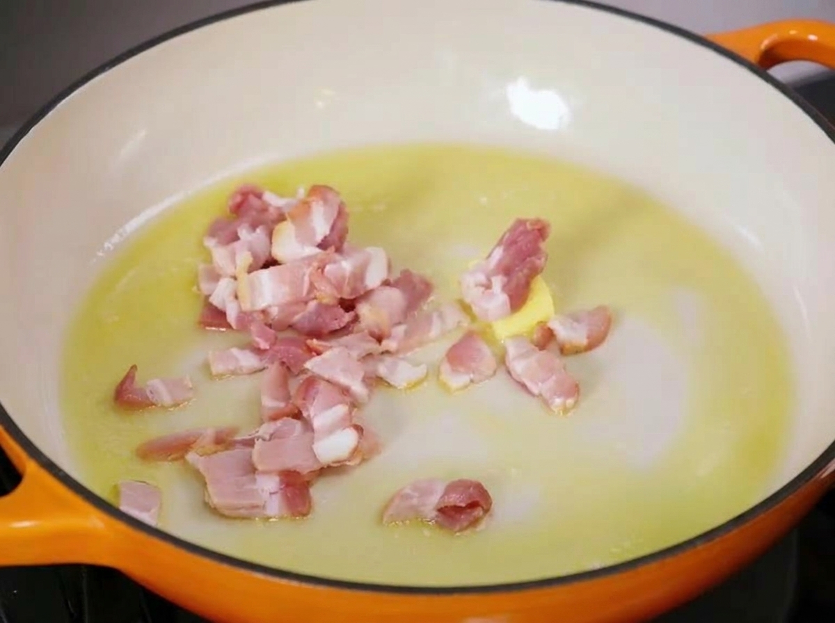 Cubetti di pancetta cruda sfrigolano in una padella calda con burro fuso e olio doliva.