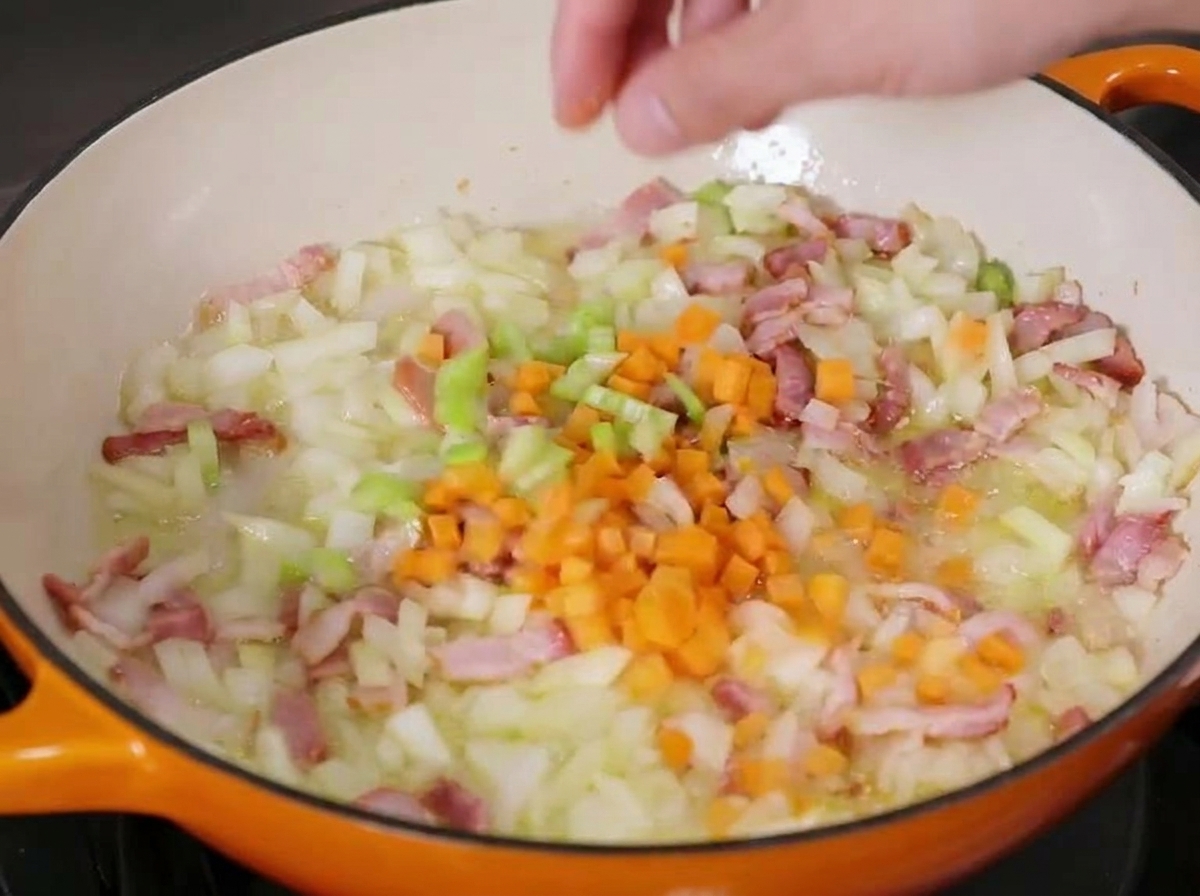 Carote a cubetti versate in una padella in ghisa con cipolle, sedano e pancetta leggermente rosolati.