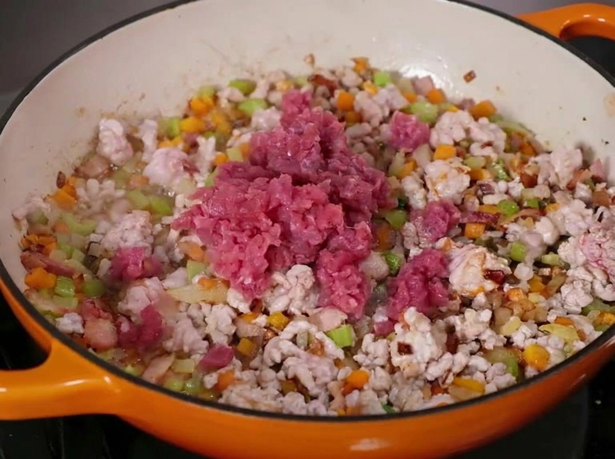 Carne di manzo e maiale macinata in cottura con verdure a cubetti in una capiente pentola in ghisa smaltata.