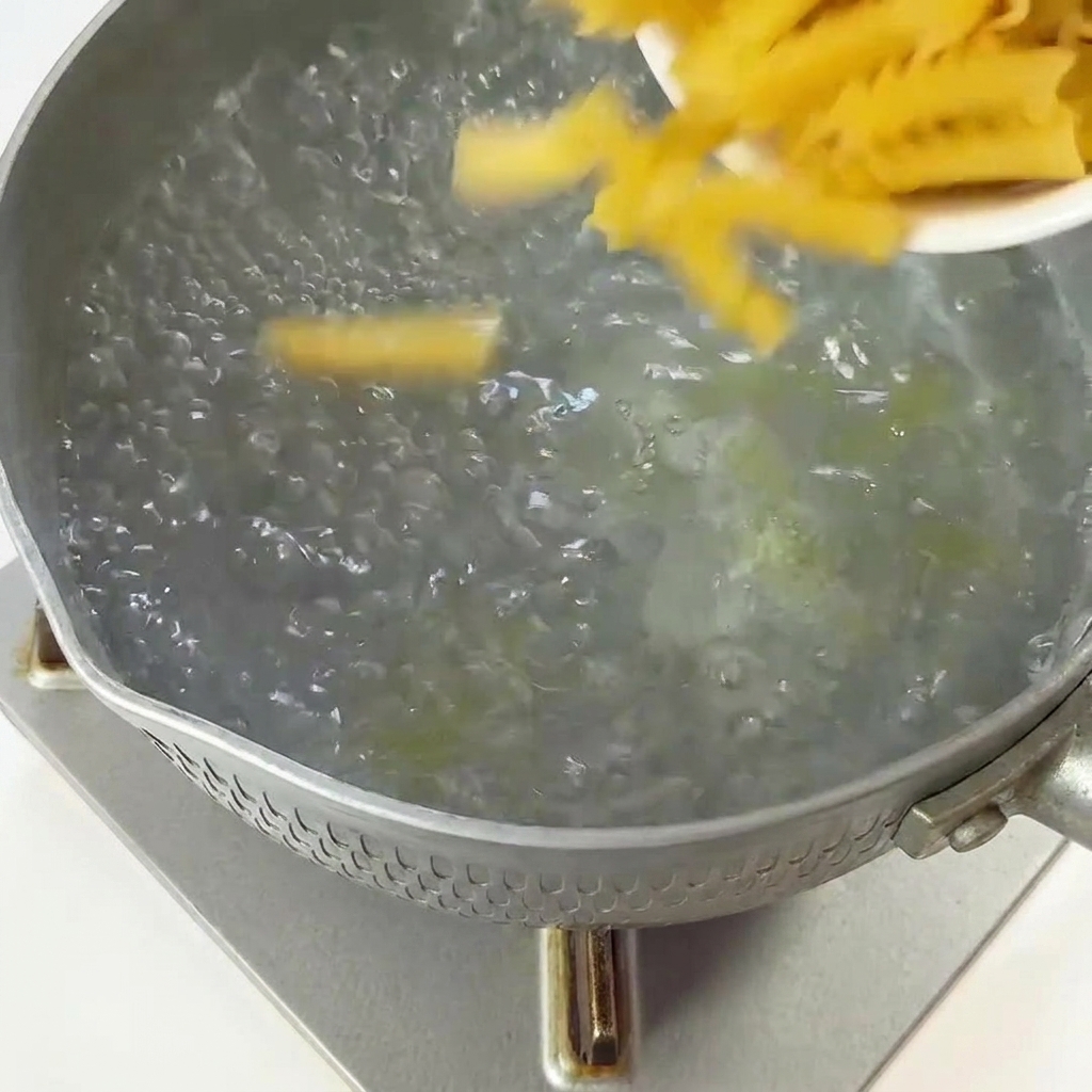 Fusilli secchi versati da un piccolo piatto in una pentola dacqua bollente.