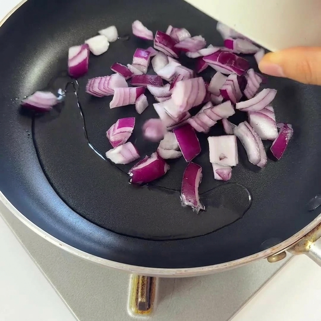 Cipolle rosse tritate che soffriggono in una padella con olio caldo e scintillante.