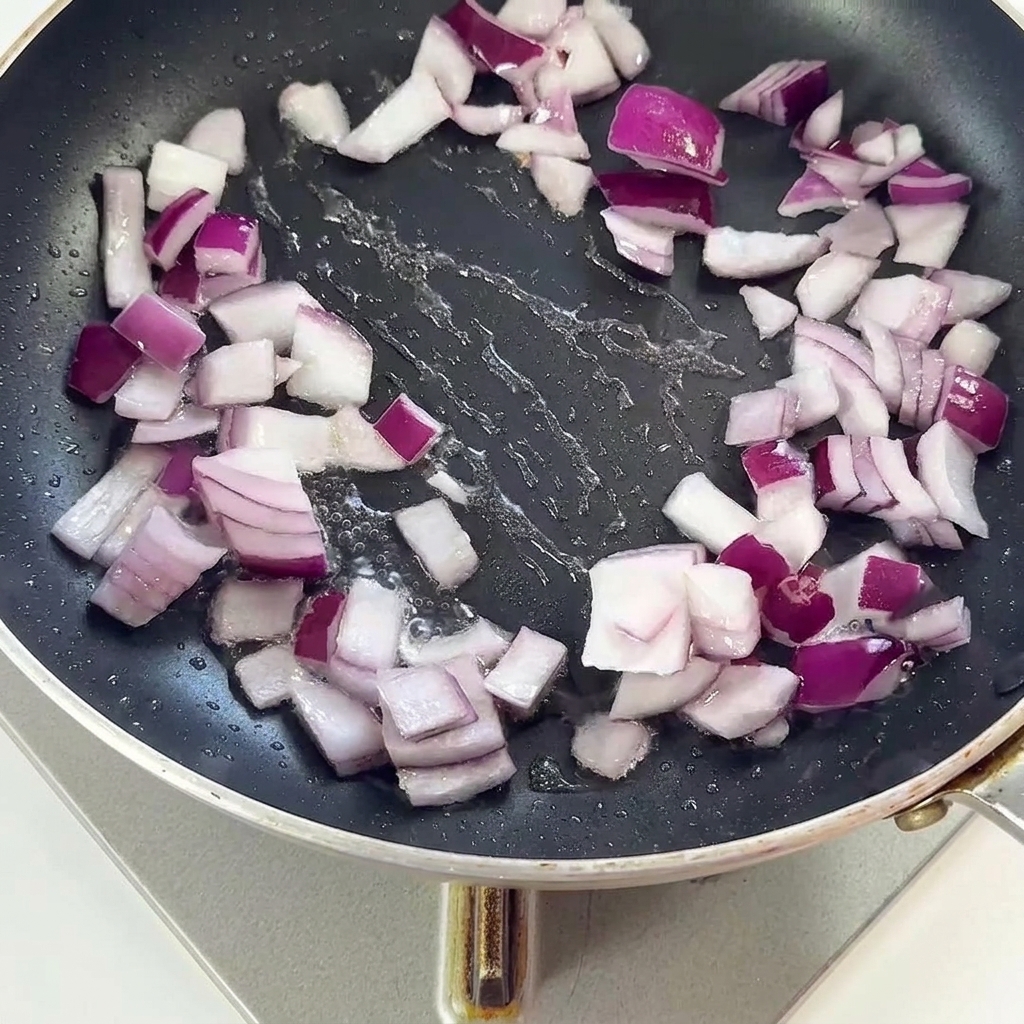 Pezzetti di bacon e cipolle rosse saltati insieme in una padella nera.