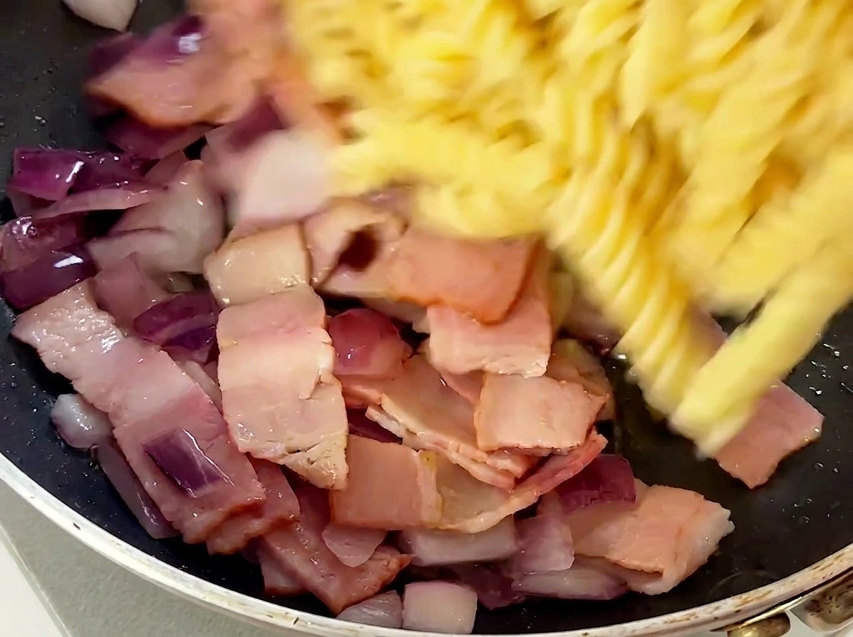 Fusilli cotti aggiunti nella padella con bacon e cipolle.