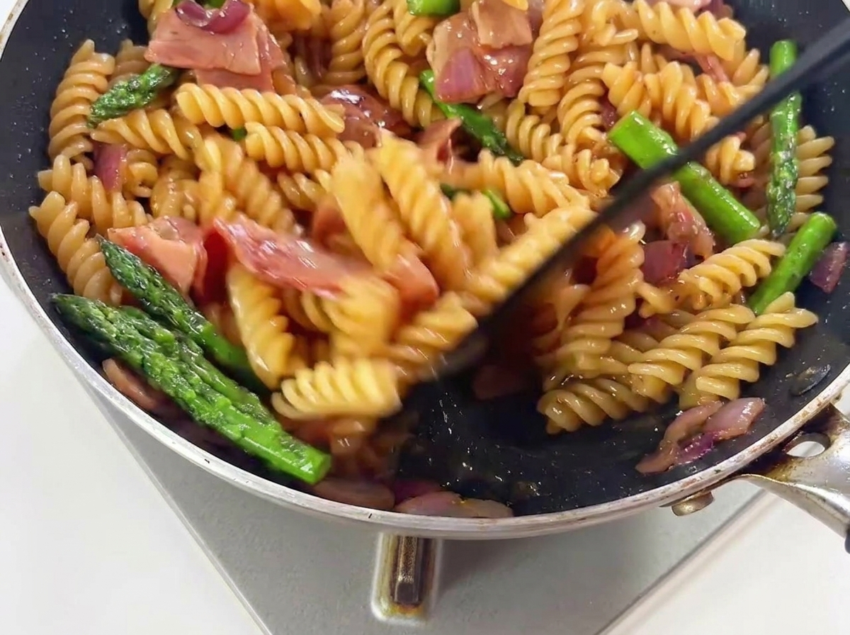 Pasta, asparagi verdi e pezzetti di bacon saltati in una padella calda per mescolarli al sugo.