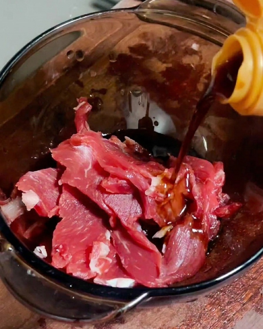 Salsa di soia versata su fette di manzo crudo in una ciotola di vetro.
