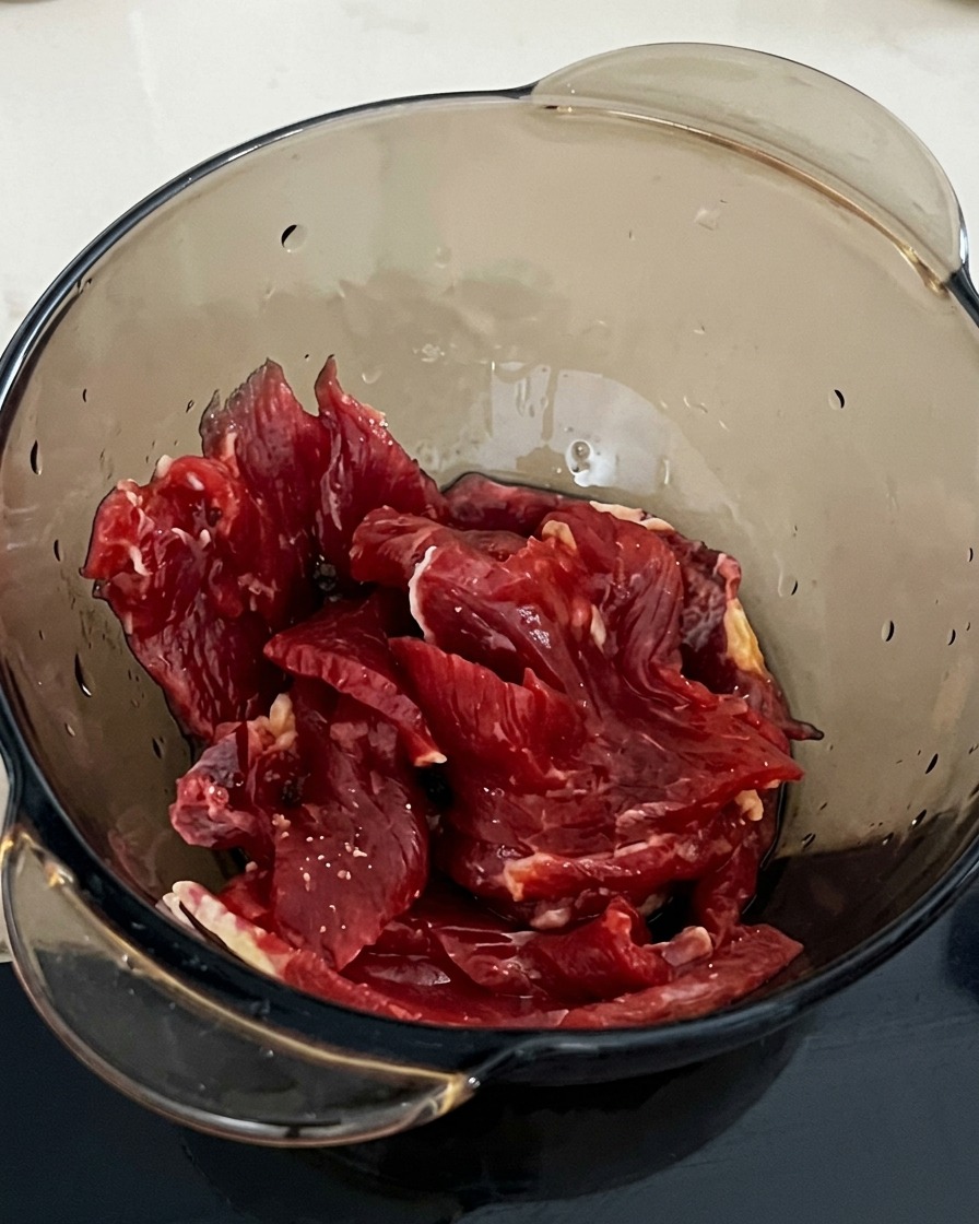 Un cucchiaio di fecola aggiunto alla ciotola con manzo e salsa di soia.