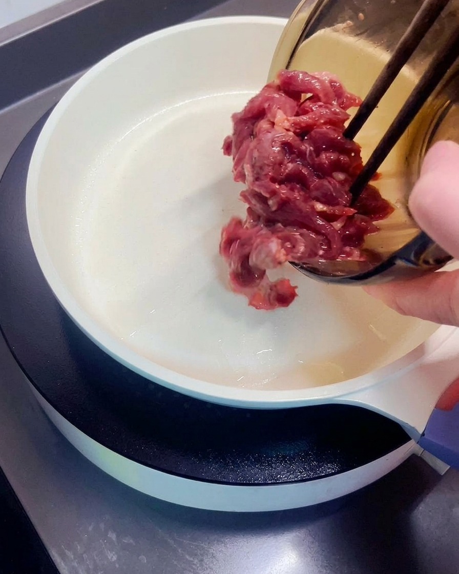Pezzi di manzo marinato trasferiti da una ciotola in una padella calda.