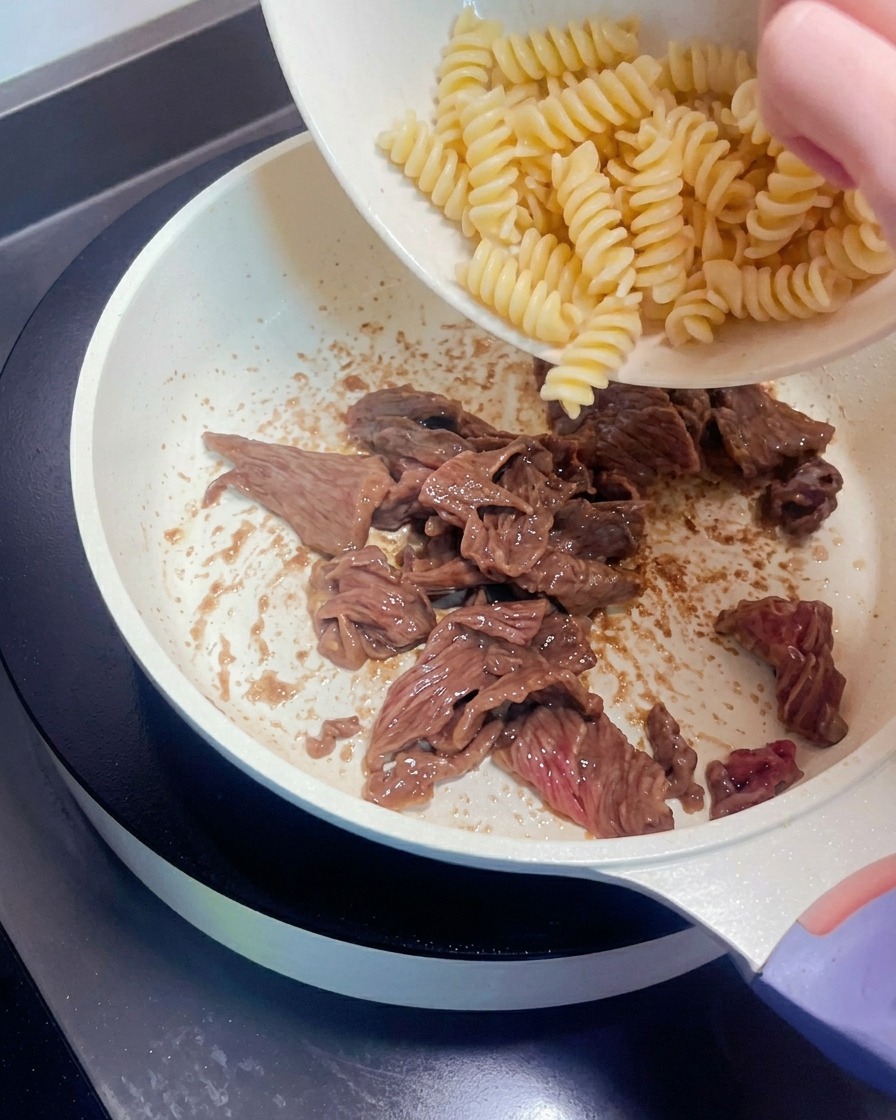 Fusilli trasferiti da una ciotola nella padella con le strisce di manzo.