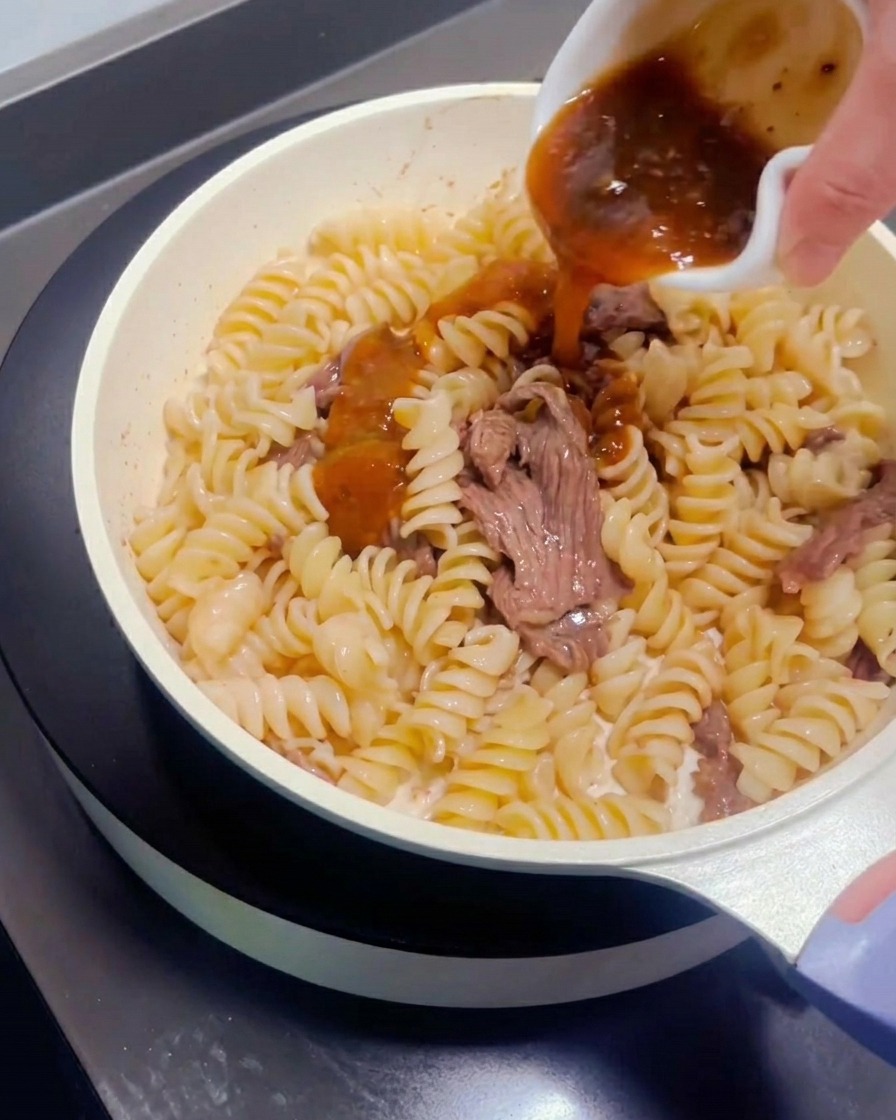 Salsa per pasta versata da una ciotolina sul manzo e la pasta.