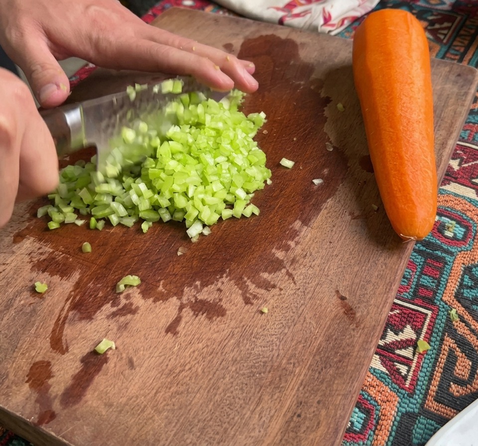 Sedano e carote finemente tritati su un tagliere di legno accanto a una carota intera.