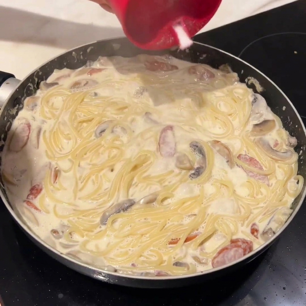 Spaghetti aggiunti alla salsa cremosa in padella.