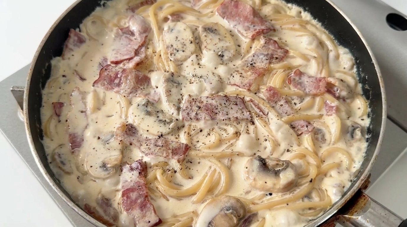 Spaghetti cremosi con funghi e pancetta, serviti caldi con una generosa spolverata di pepe nero.