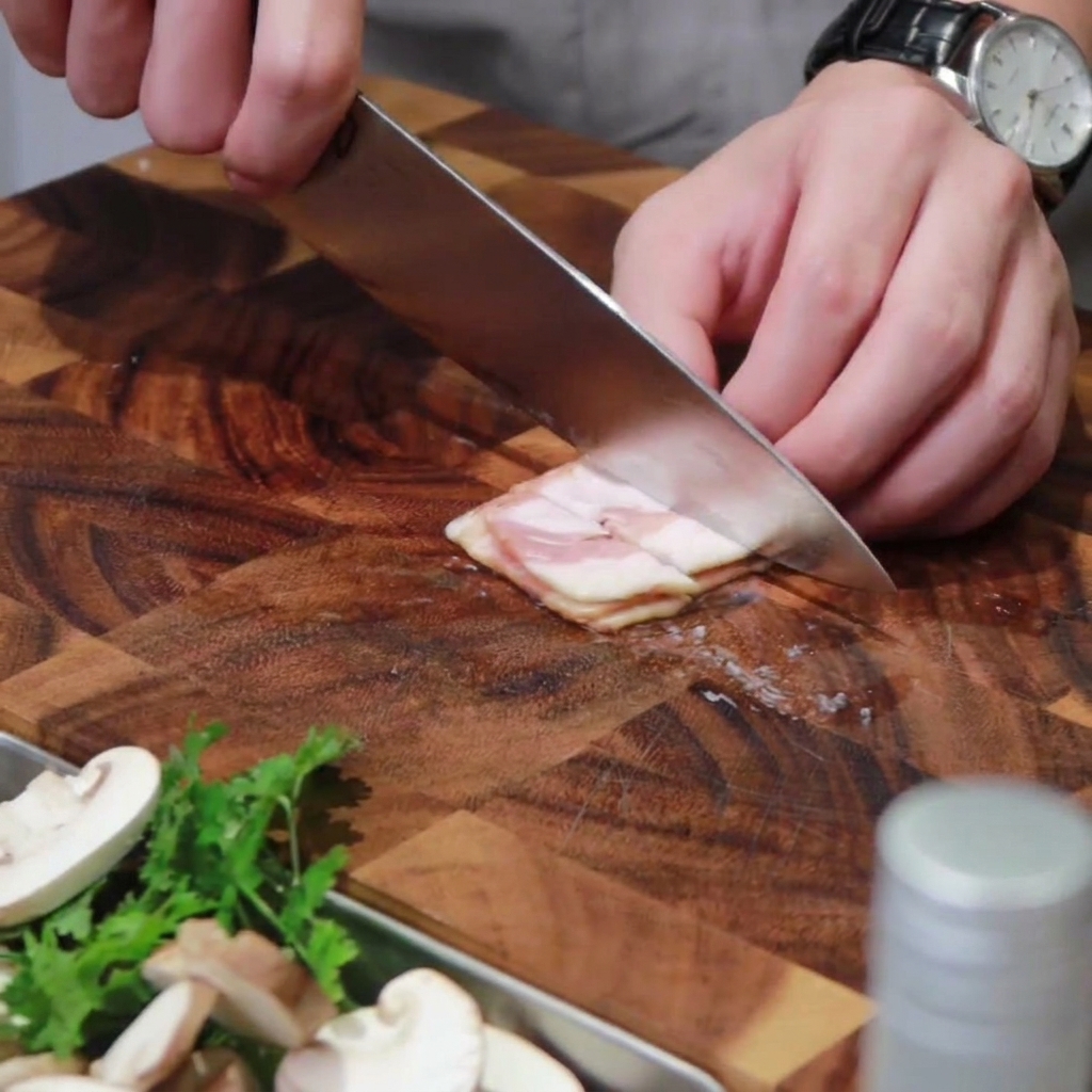 Fette di bacon tagliate a listarelle su un tagliere di legno.