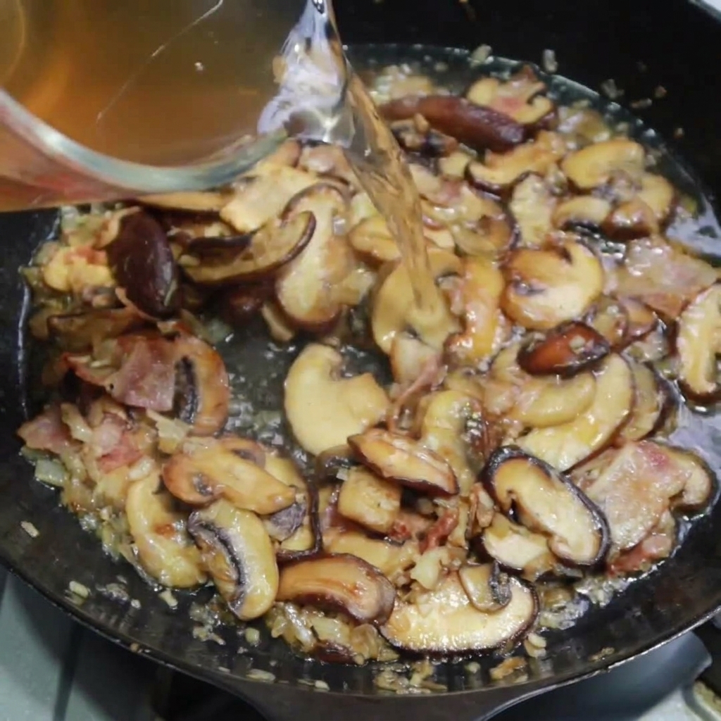 Brodo di pollo versato nella padella per sfumare funghi e bacon.