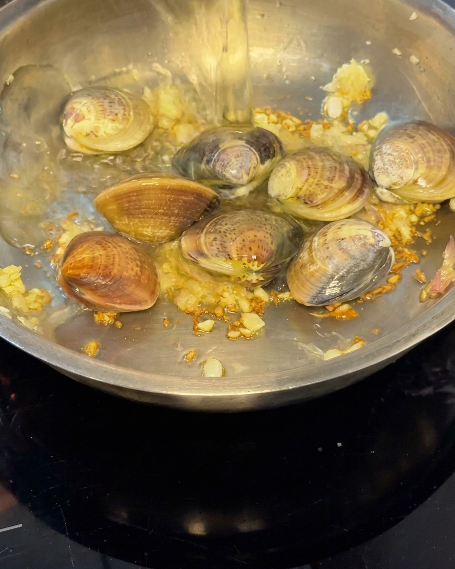Vino bianco versato in padella sulle vongole per creare vapore.