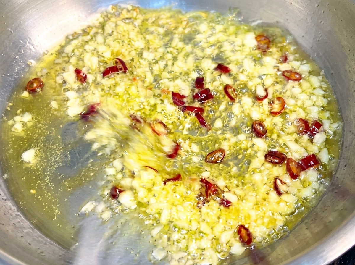 Pasta saltata in padella con aglio dorato e peperoncino, ricoperta da una salsa lucida ed emulsionata.