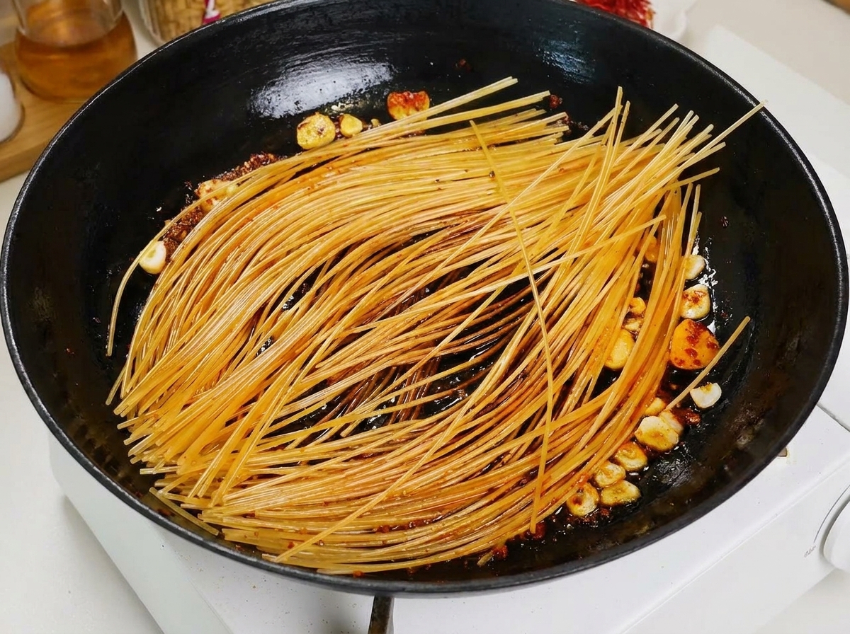 Un mestolo versa brodo di pomodoro sulla pasta in cottura.