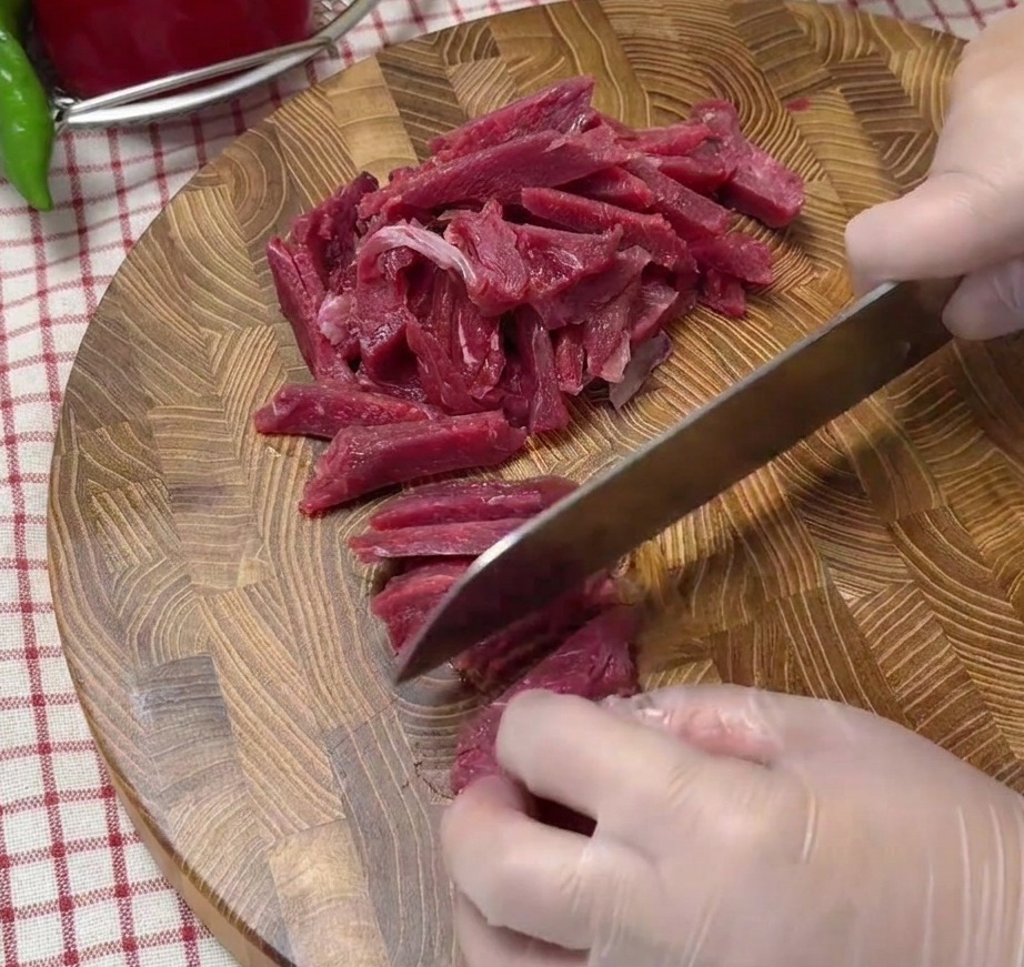 Striscioline di manzo crudo tagliate sottili disposte su un tagliere di legno.