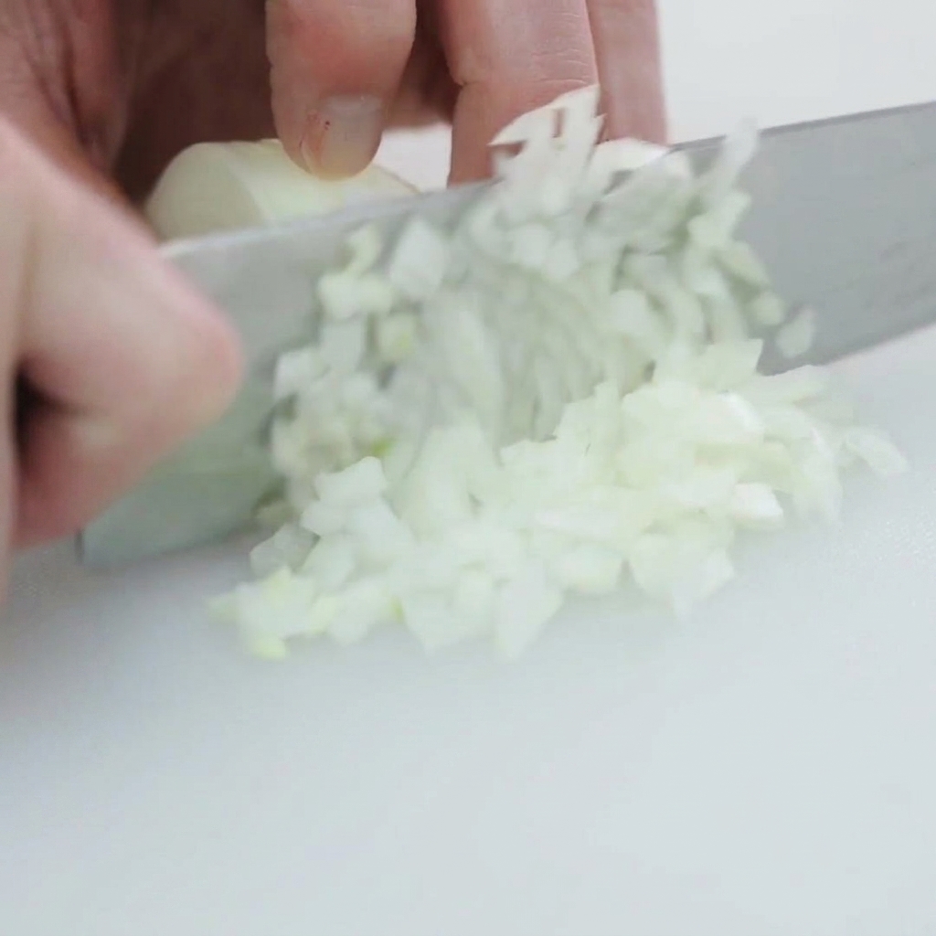 Una cipolla bianca tagliata a cubetti piccoli e uniformi su un tagliere.