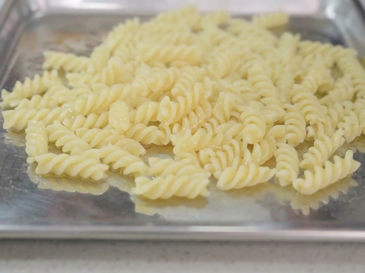 Pasta cotta su un vassoio di metallo condita con un filo dolio.
