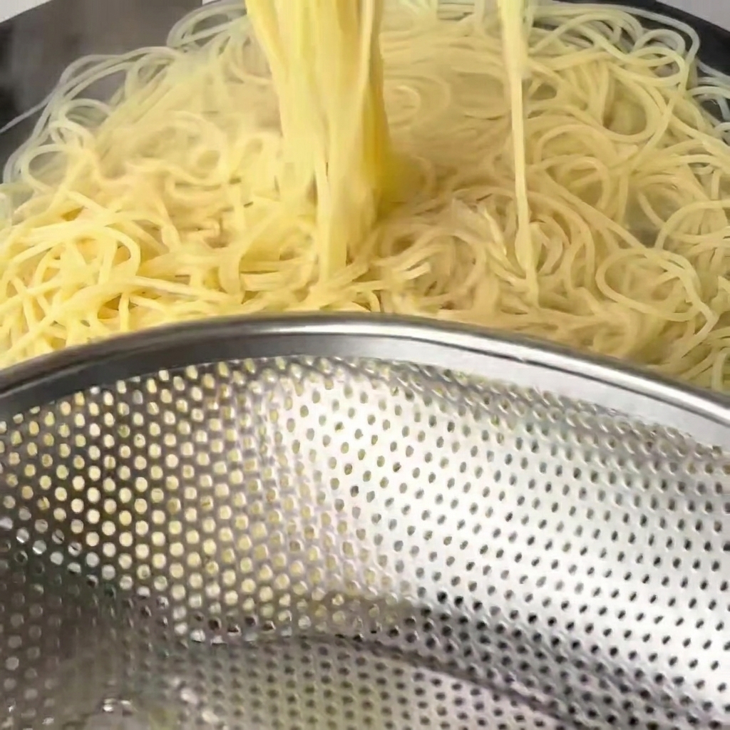 Spaghetti cotti sollevati dal wok con bacchette di legno.