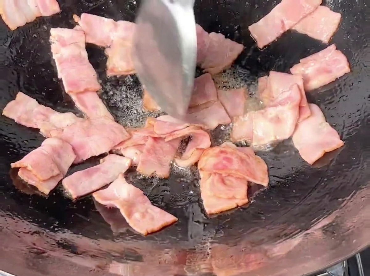 Pezzetti di pancetta rettangolari saltati nel wok con una spatola metallica.