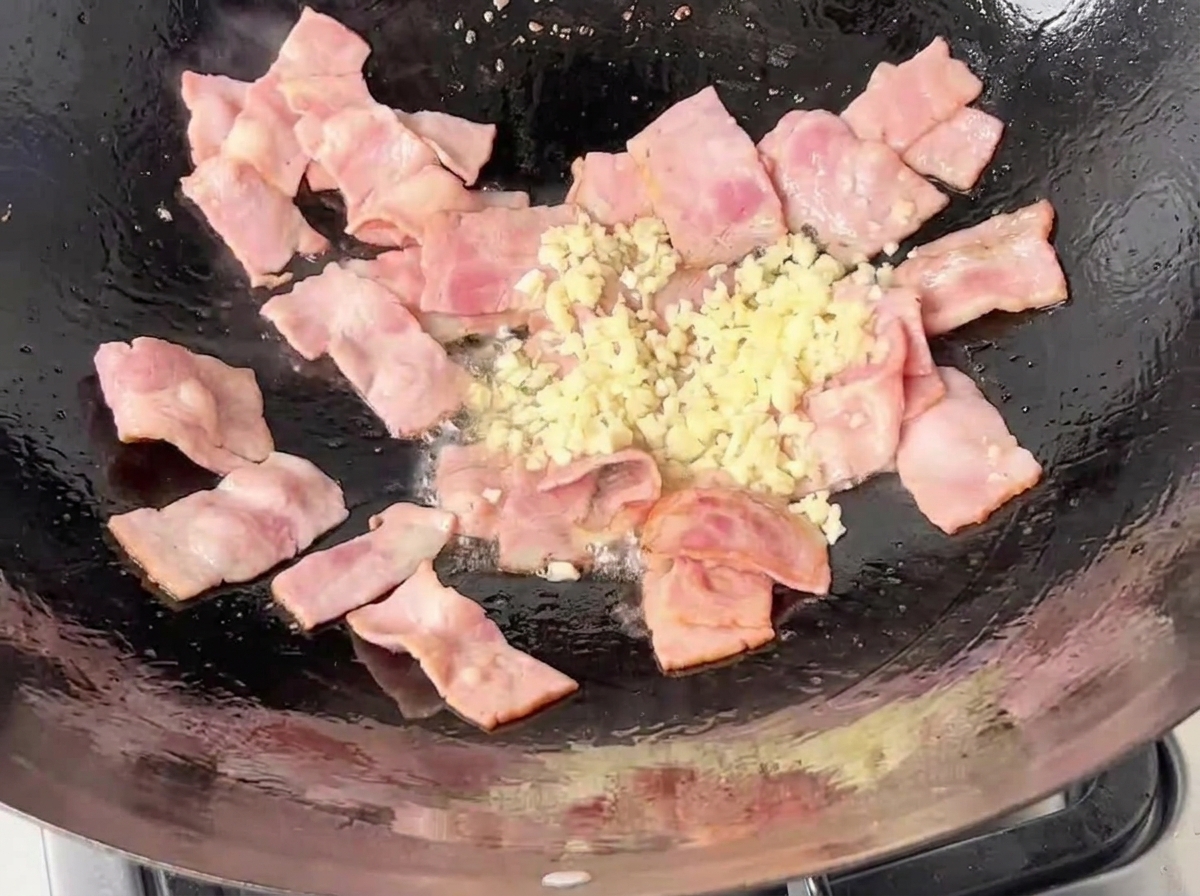 Aglio tritato aggiunto nel wok con la pancetta sfrigolante.