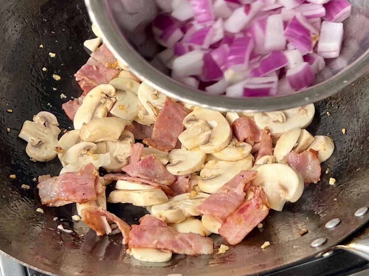 Cipolla rossa a dadini saltata insieme ai funghi e alla pancetta nel wok.