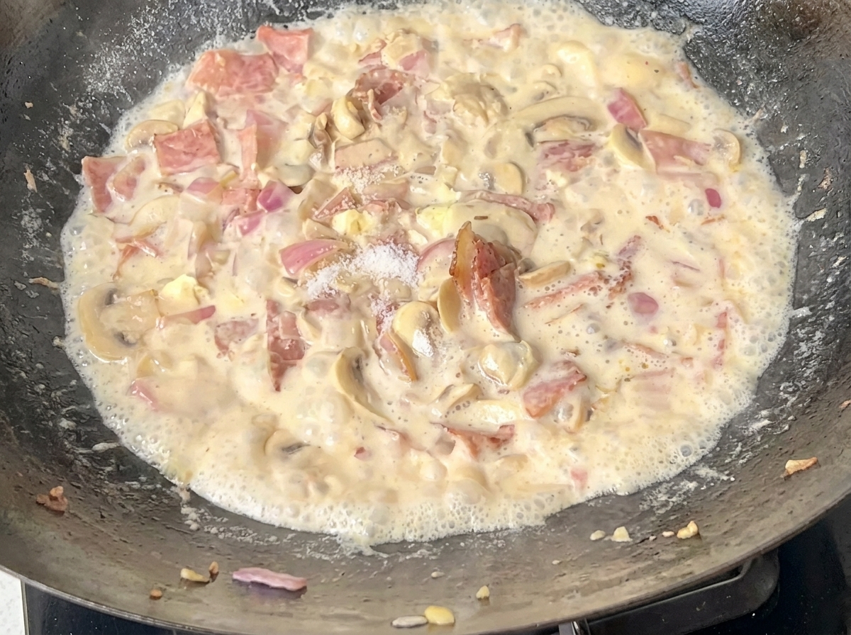 Spaghetti aggiunti alla salsa cremosa nel wok.