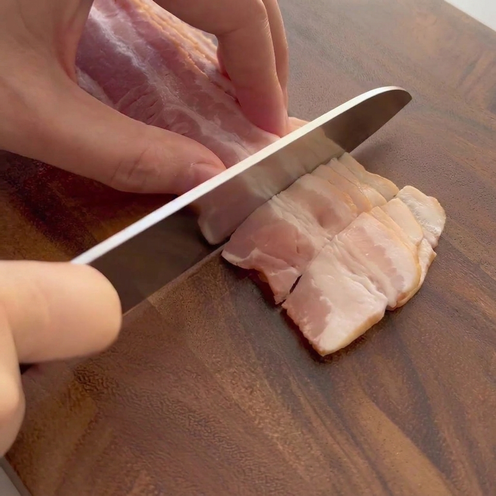 Fette di pancetta cruda tagliate su un tagliere di legno.