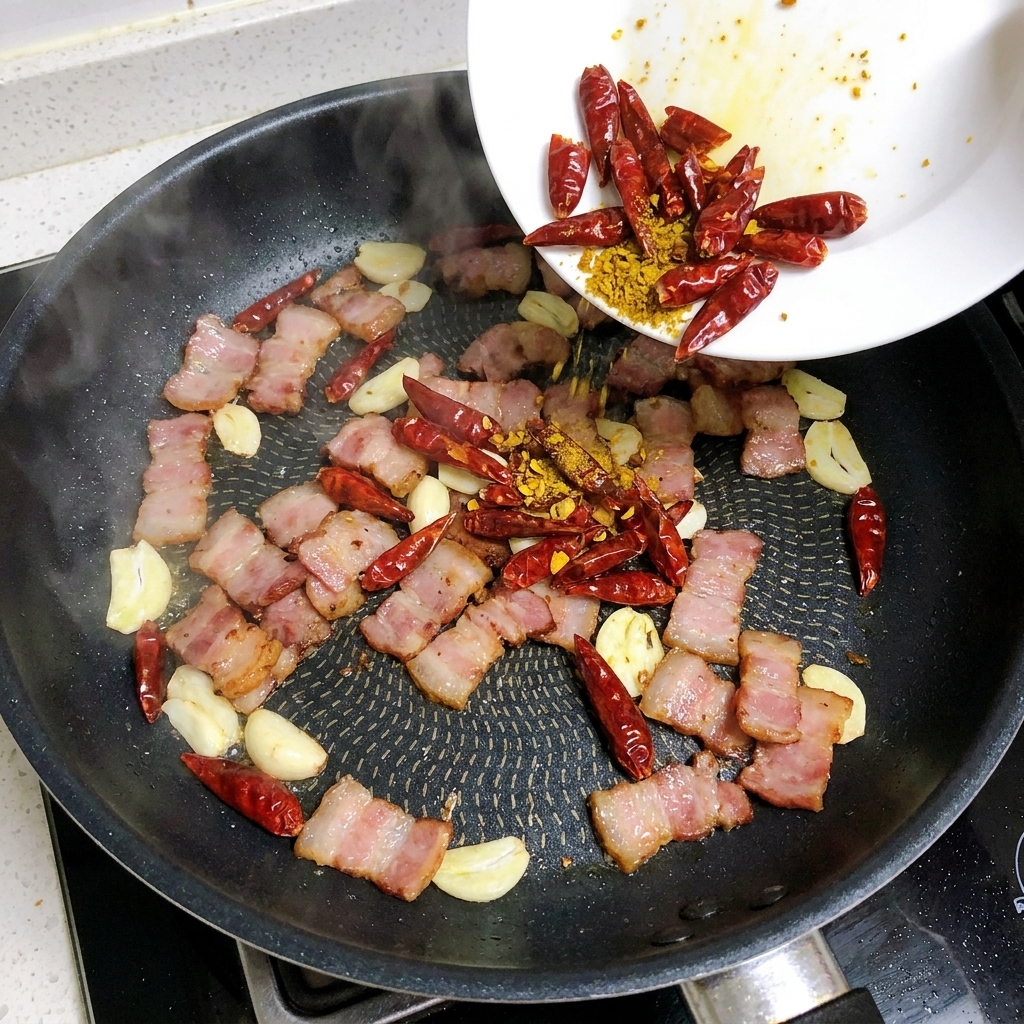 Fette di aglio e peperoncini secchi aggiunti in padella con la pancetta che soffrigge.