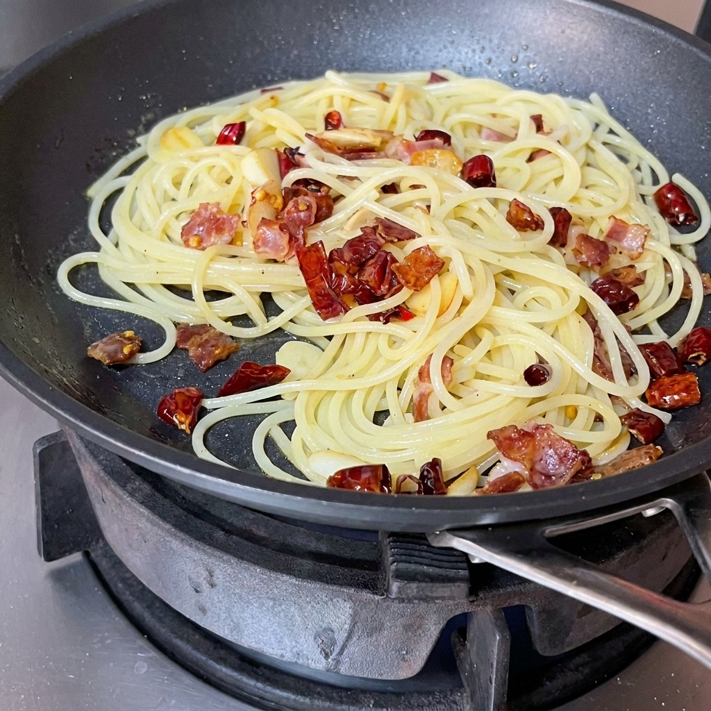 Spaghetti, pancetta e aromi saltati insieme in una padella con una spatola rossa.