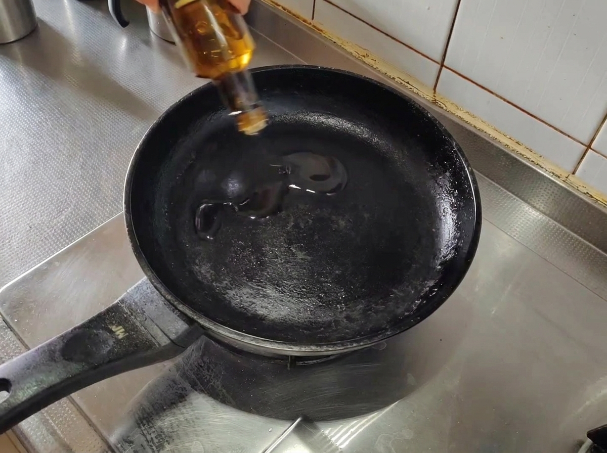 Olio doliva versato in una padella nera vuota preriscaldata su un fornello.