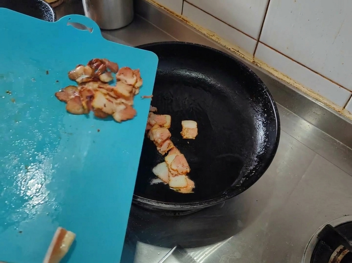Strisce di pancetta cruda aggiunte in una padella calda con olio doliva.