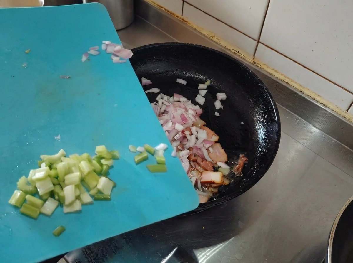 Scalogno e sedano tritati aggiunti in padella con la pancetta rosolata.
