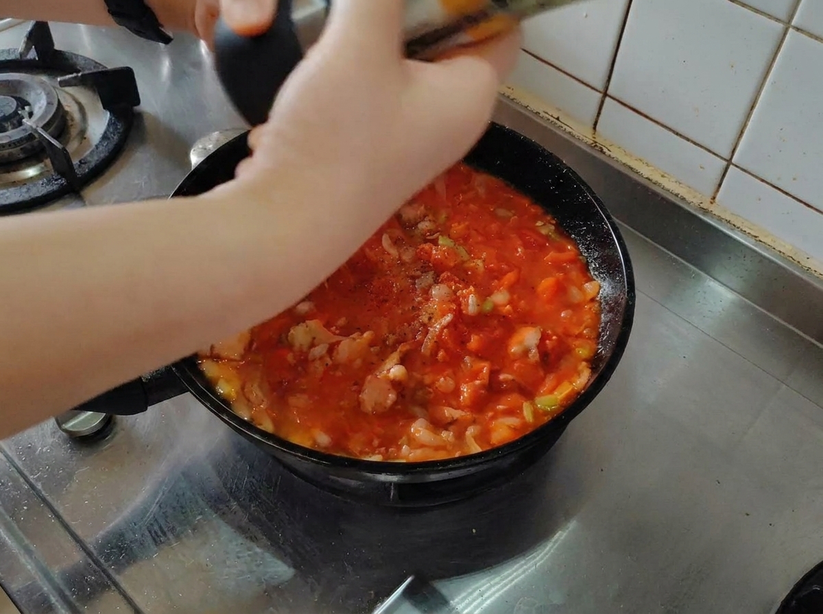 Pepe nero fresco macinato sopra un sugo di pomodoro e pancetta in una padella nera.