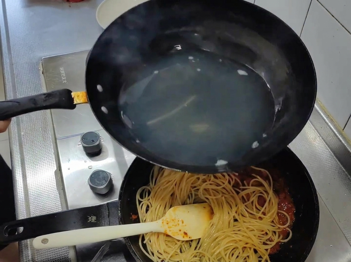 Spaghetti cotti spostati dallacqua bollente in una padella con un sugo di pomodoro rosso.