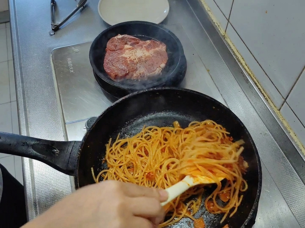 Spaghetti saltati con le pinze in una padella, ricoperti completamente da un denso sugo al pomodoro.