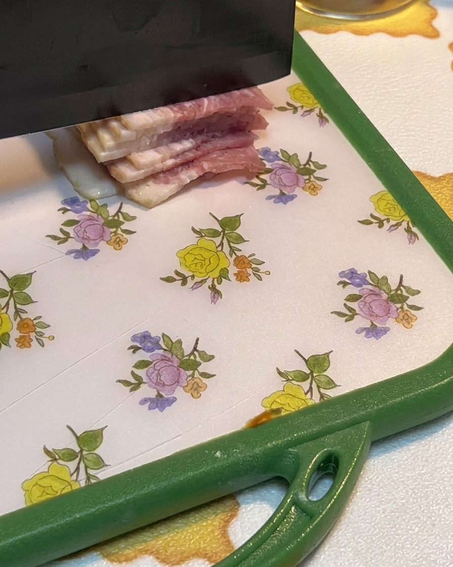 Fette di pancetta cruda tagliate a pezzetti su un tagliere.