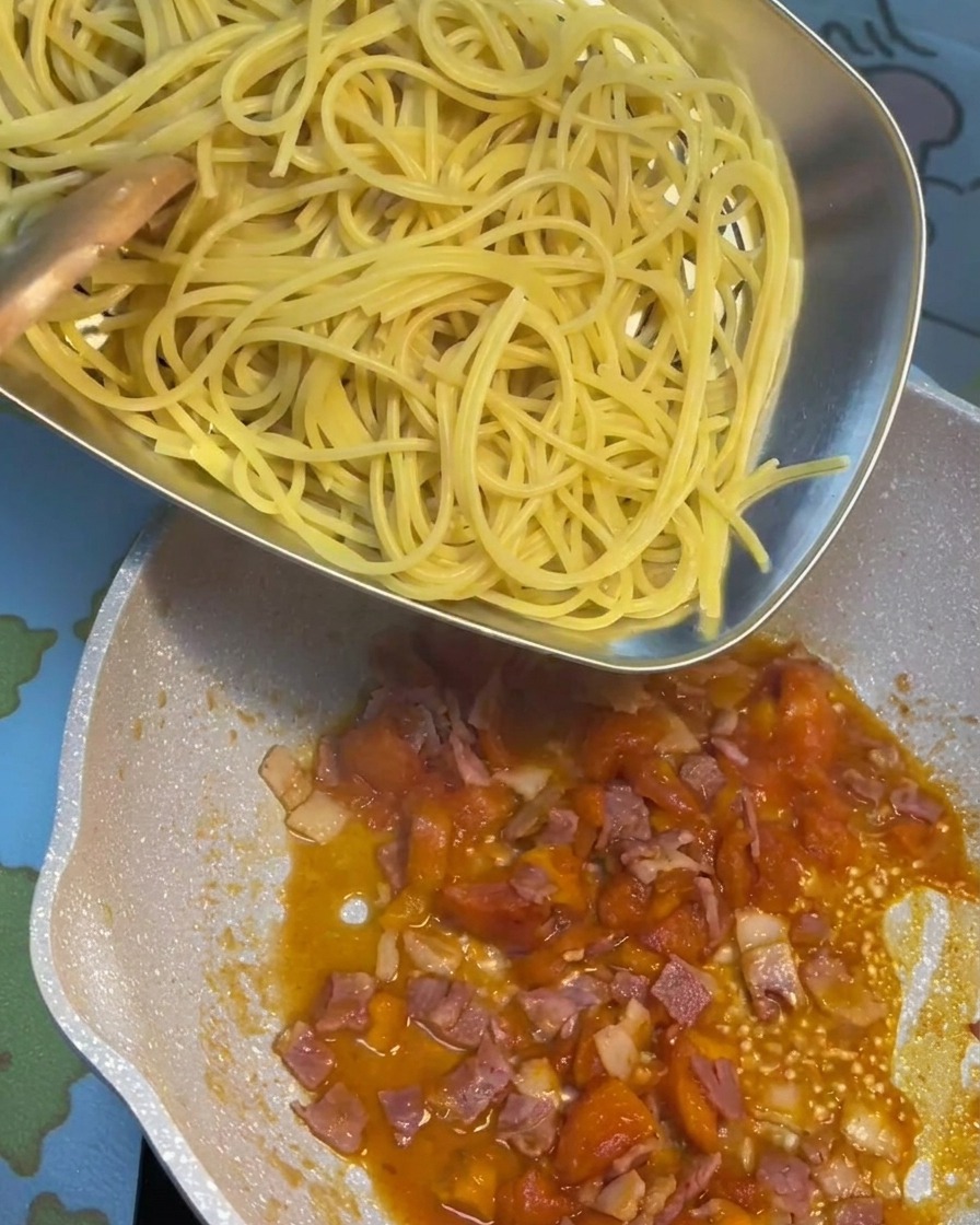 Pasta scolata aggiunta nella padella con il sugo di pomodoro e pancetta.