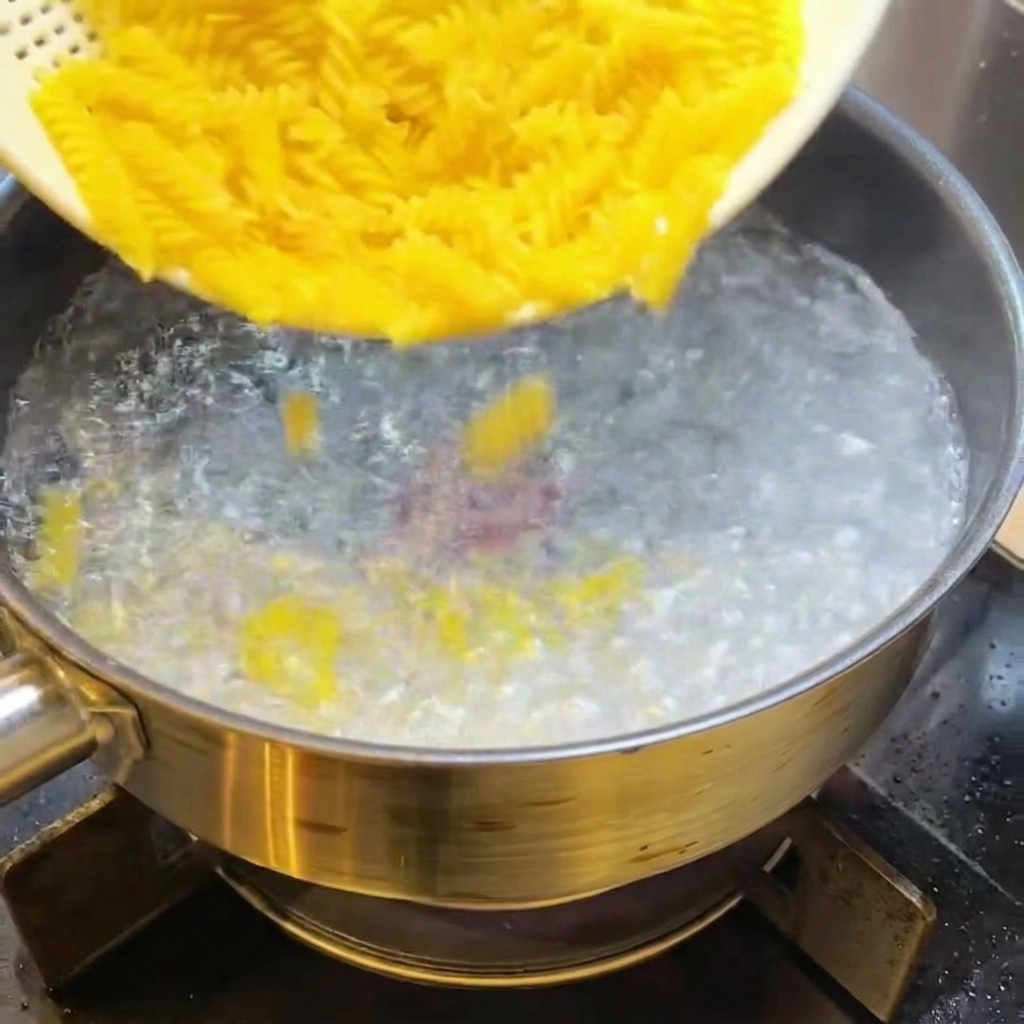 Fusilli crudi immersi in una pentola di acqua bollente.