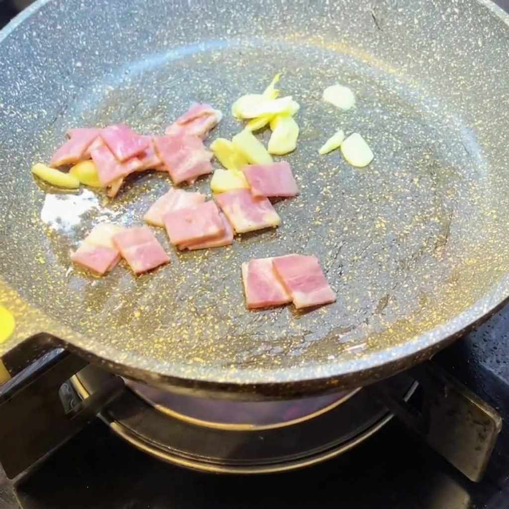 Pezzetti di pancetta che rosolano in padella con laglio.