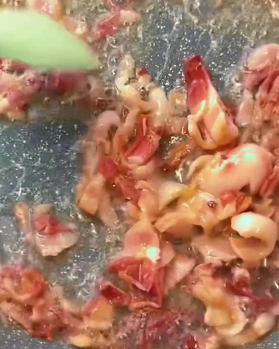 Sugo di pomodoro rosso che sobbolle in padella con pezzetti di pancetta dorata.