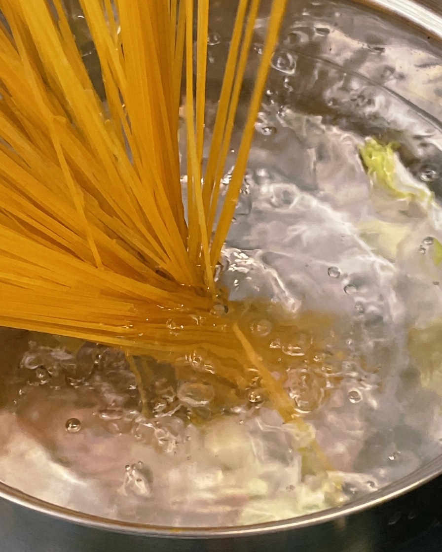 Un cucchiaio di legno mescola il sugo denso di pomodoro e pancetta in una padella.