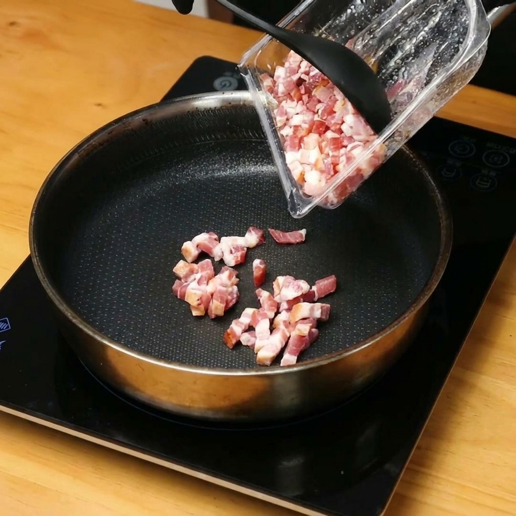 Pezzetti di pancetta che sfrigolano e rilasciano il loro grasso in una padella rovente.