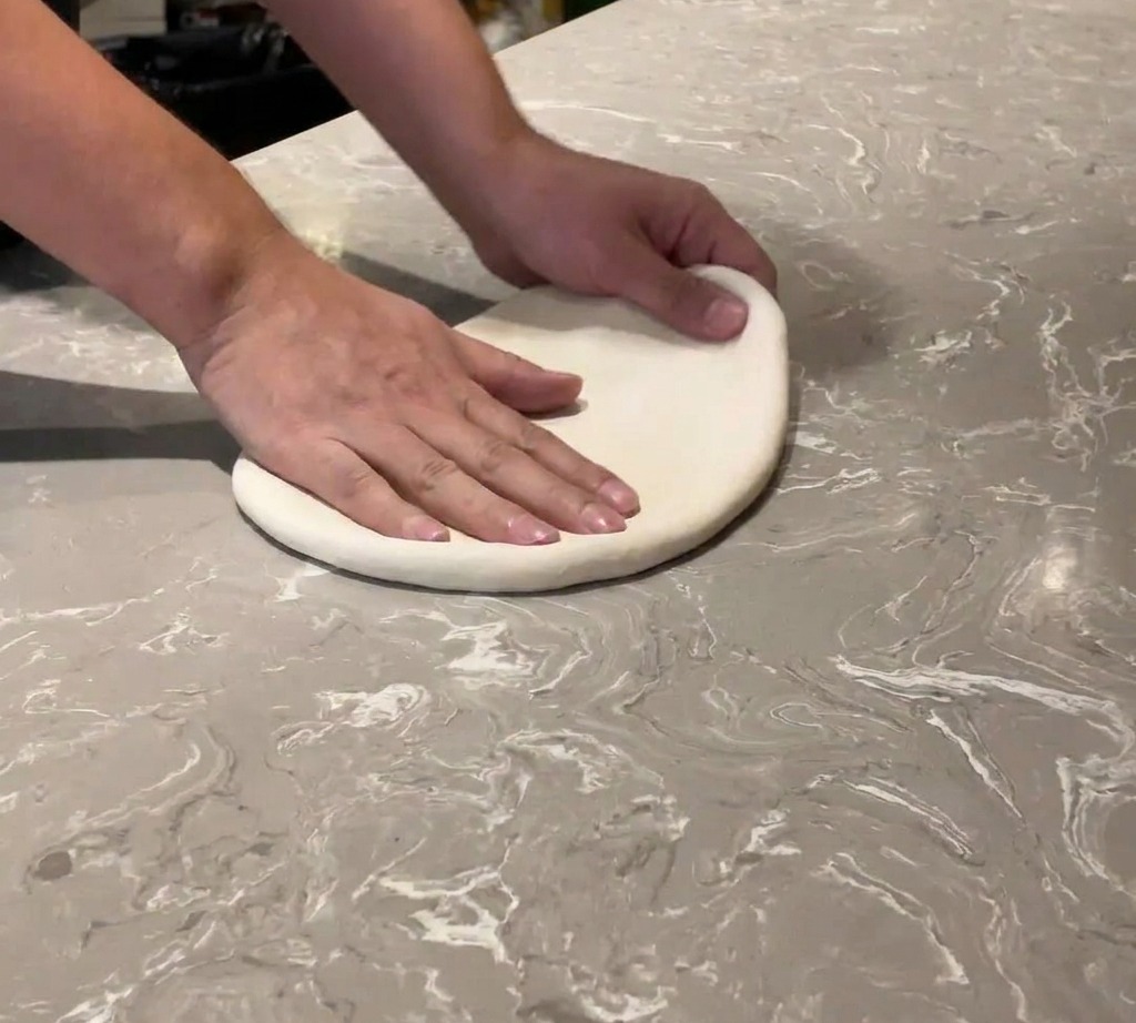 Primo piano di mani che stendono una pallina di impasto per pizza su un piano di marmo.