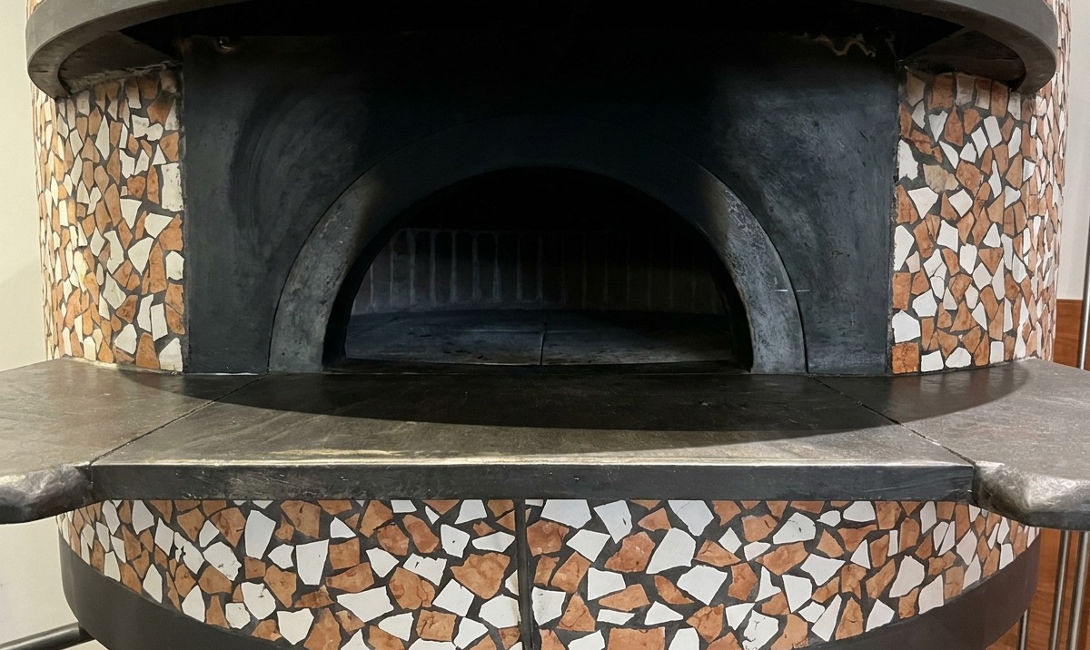 Pizza in cottura in un forno a mattoni, con il bordo che si gonfia e si colora vicino alle fiamme.