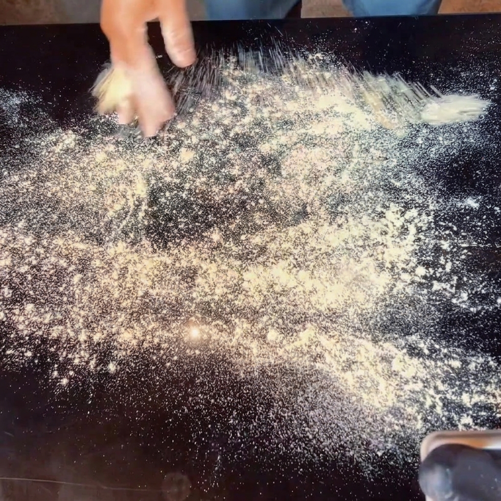 Mani che stendono limpasto per la pizza su un piano di lavoro infarinato.